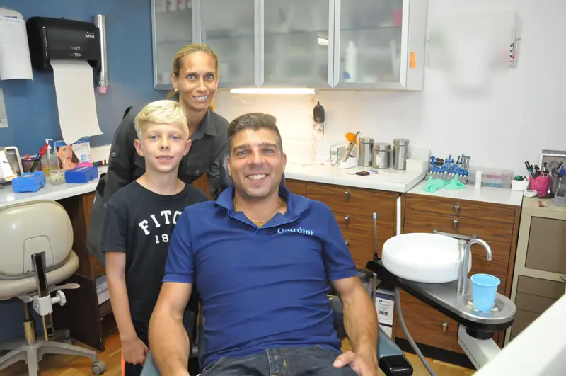 Un père et son fils posent dans la salle de soins avec une membre de l’équipe